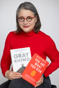 Photo of a woman in glasses holding two books, THE GRAY RHINO and YOU ARE WHAT YOU RISK