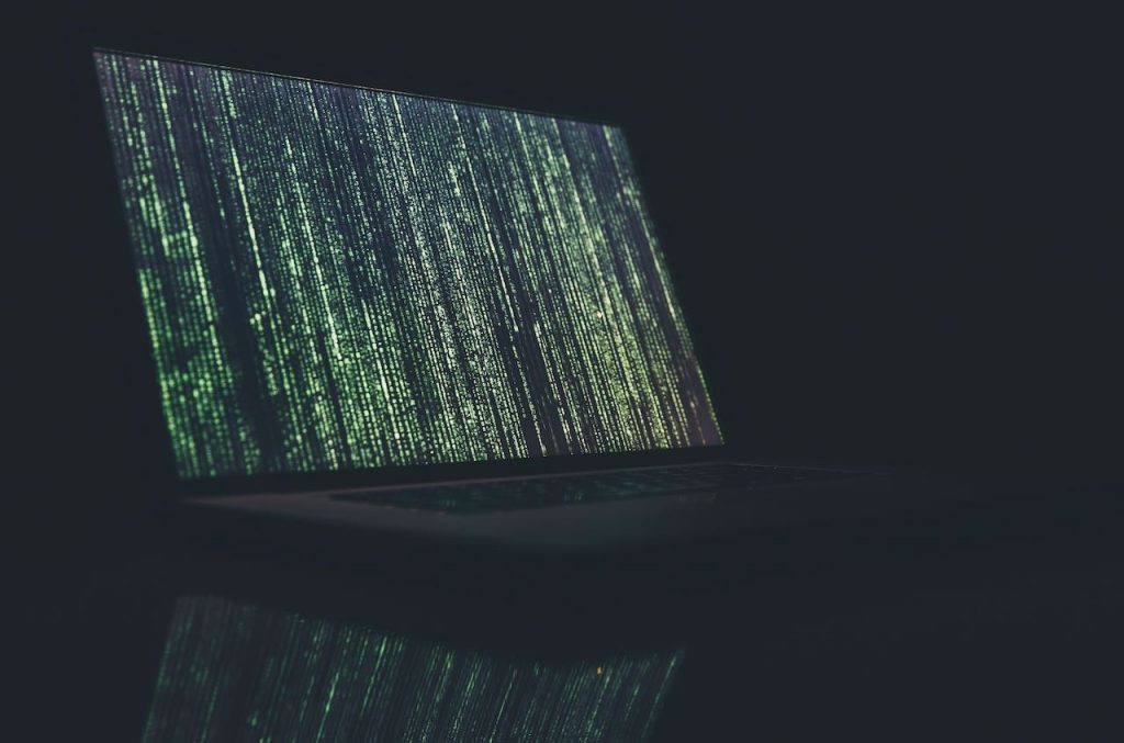 green-grey code filling the screen of a laptop in a dark room